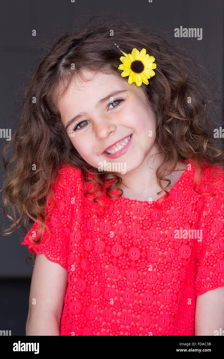 Portrait d'une jeune fille avec un fond gris. Elle porte des vêtements décontractés avec une fleur dans ses cheveux et souriant à la cam Banque D'Images