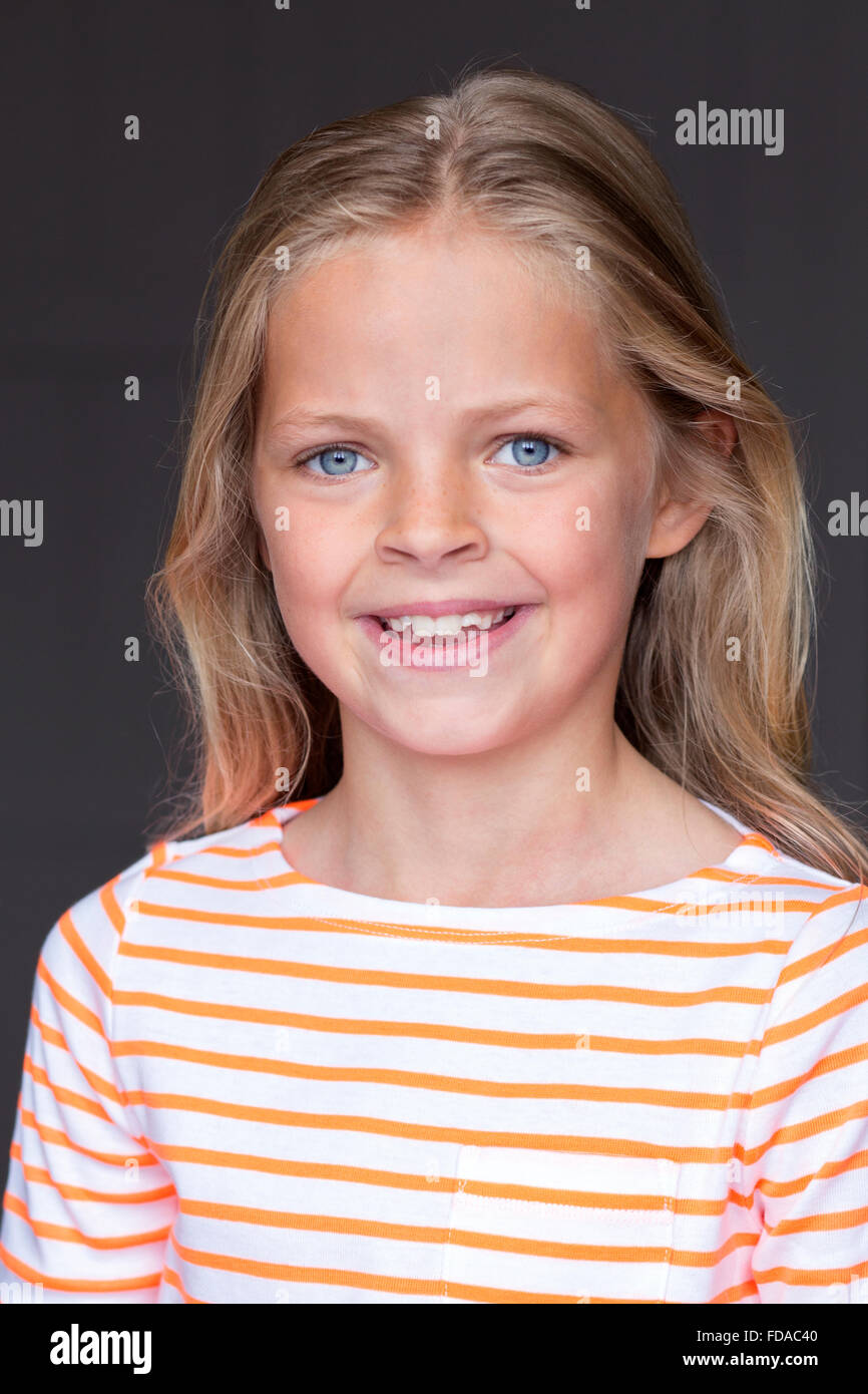 Portrait d'une jeune fille sur un fond gris. Elle est à la recherche à la caméra et sourit. Banque D'Images