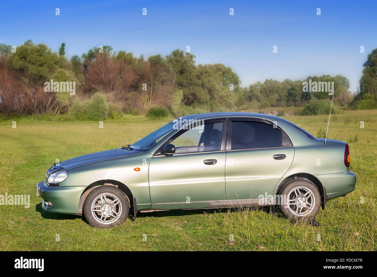 Sur la pelouse verte par la rivière est une voiture d'une couleur vert clair. Banque D'Images