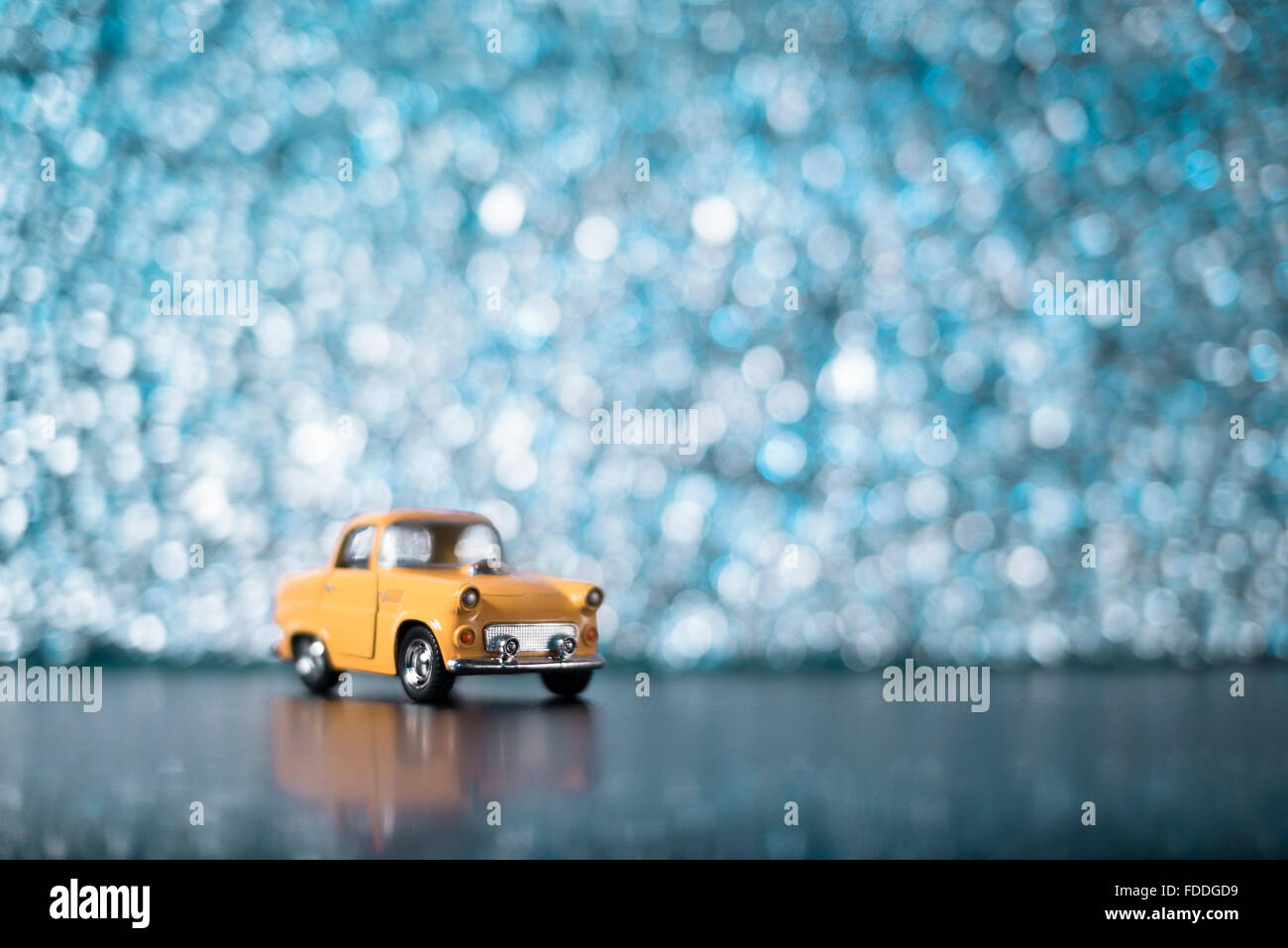 Une petite voiture jaune sur un arrière-plan flou d'turqouise. Banque D'Images