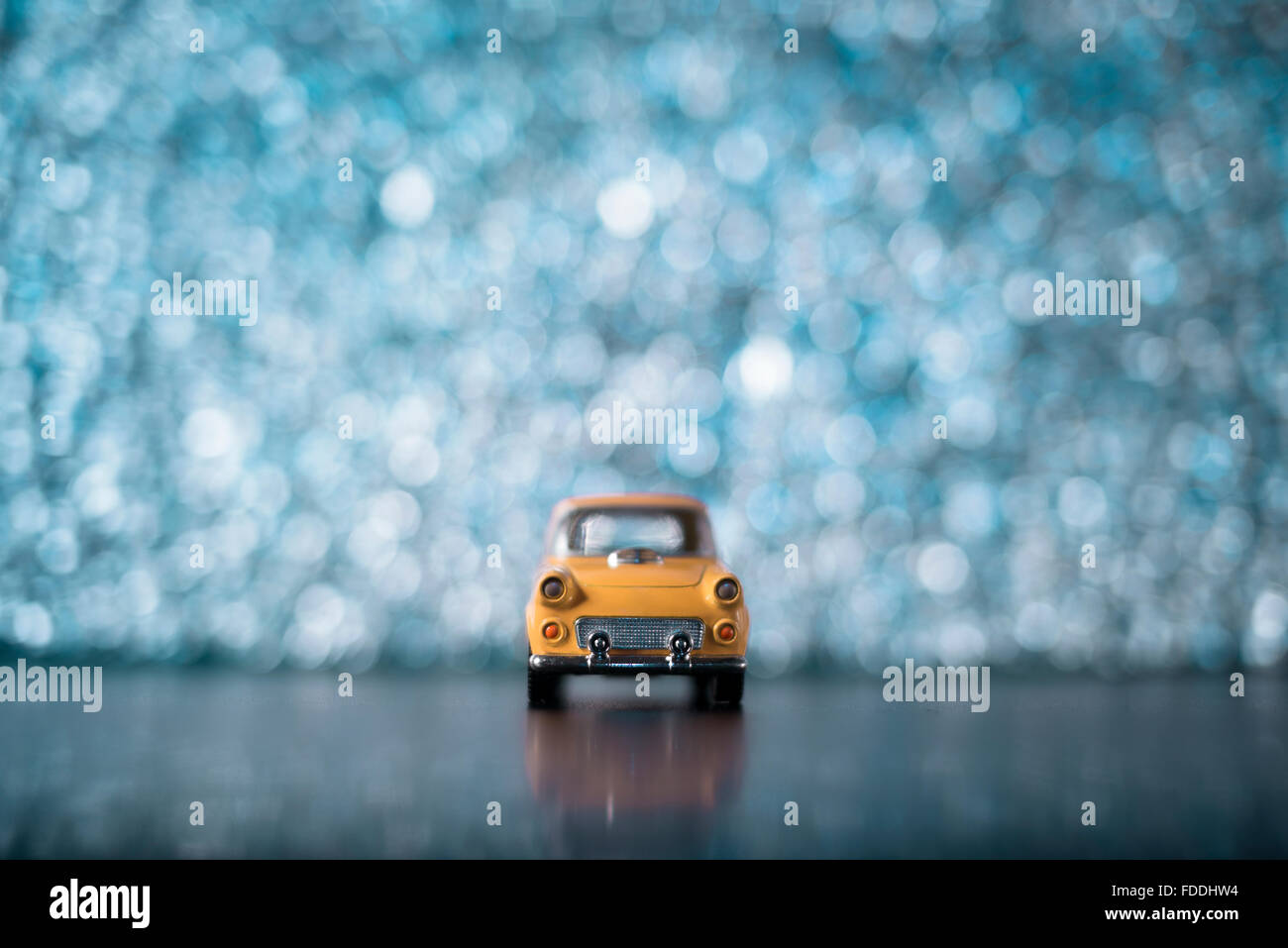 Une petite voiture jaune sur un arrière-plan flou d'turqouise. Banque D'Images