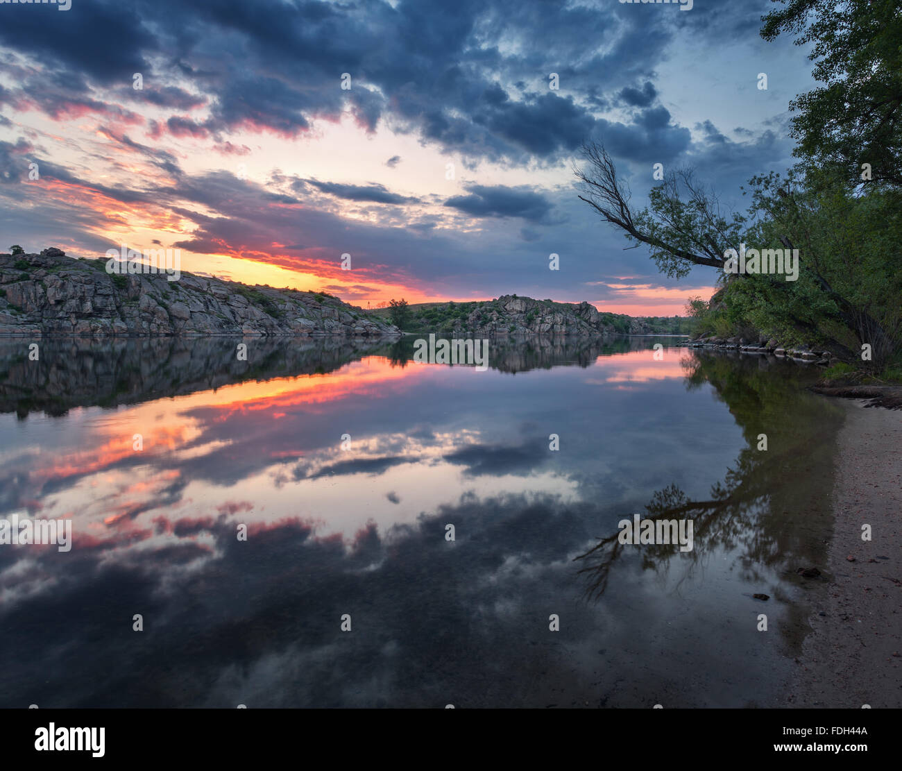 Beau paysage. De soleil colorés sur la plage avec des arbres et des rochers. Lake avec les nuages reflètent dans l'eau. Banque D'Images