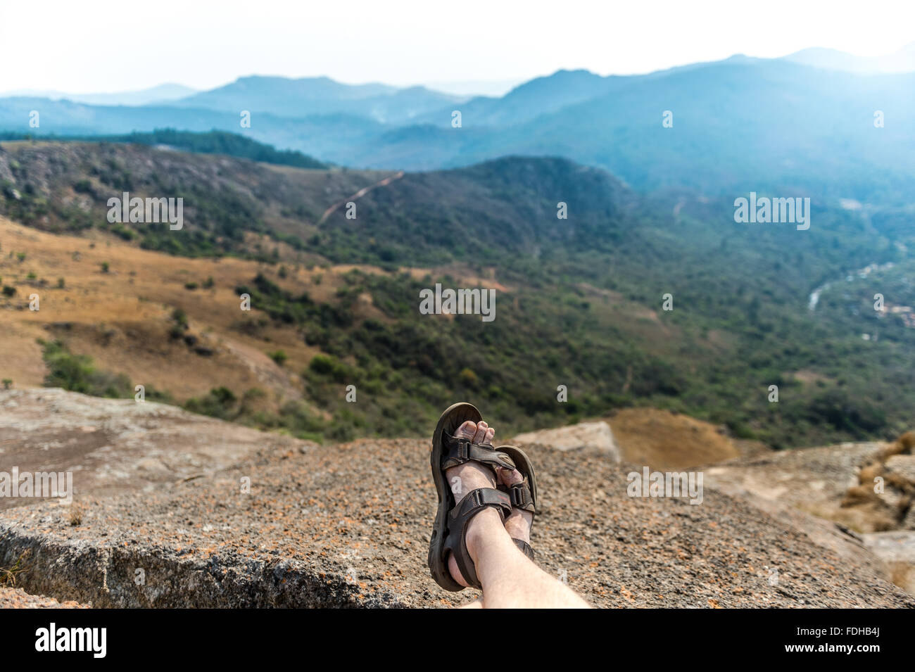 Les pieds de l'homme allongé en face d'un paysage de montagne à l'Mlilwane Wildlife Sanctuary au Swaziland, Afrique. Banque D'Images