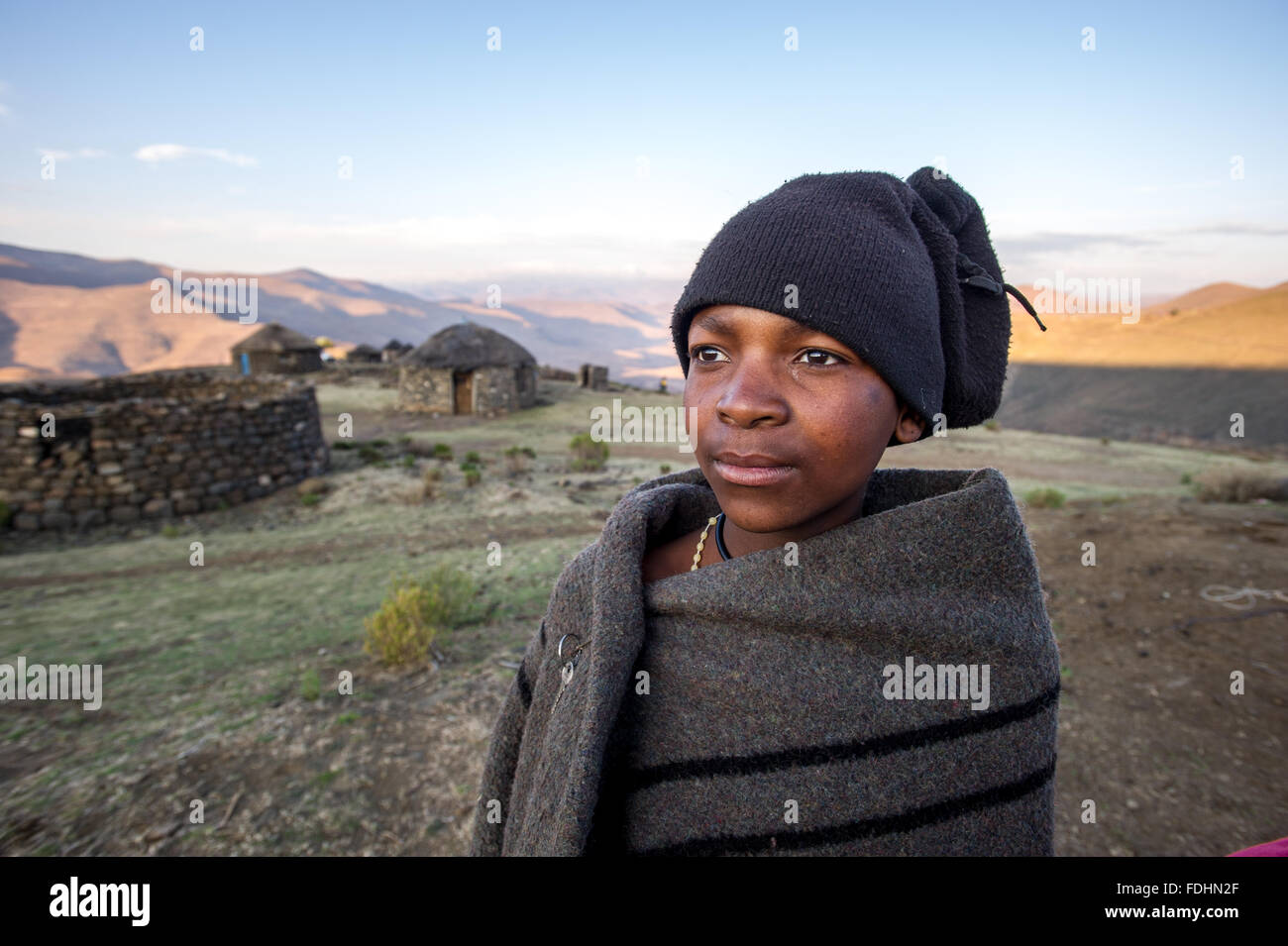 Jeune garçon enveloppé dans une couverture près d'une cabane en pierre au Lesotho, l'Afrique Banque D'Images