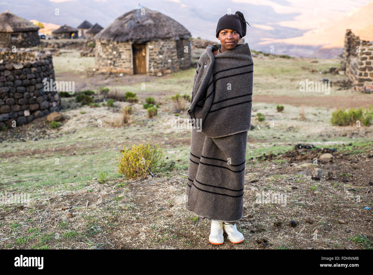 Jeune garçon enveloppé dans une couverture près d'une cabane en pierre au Lesotho, l'Afrique Banque D'Images