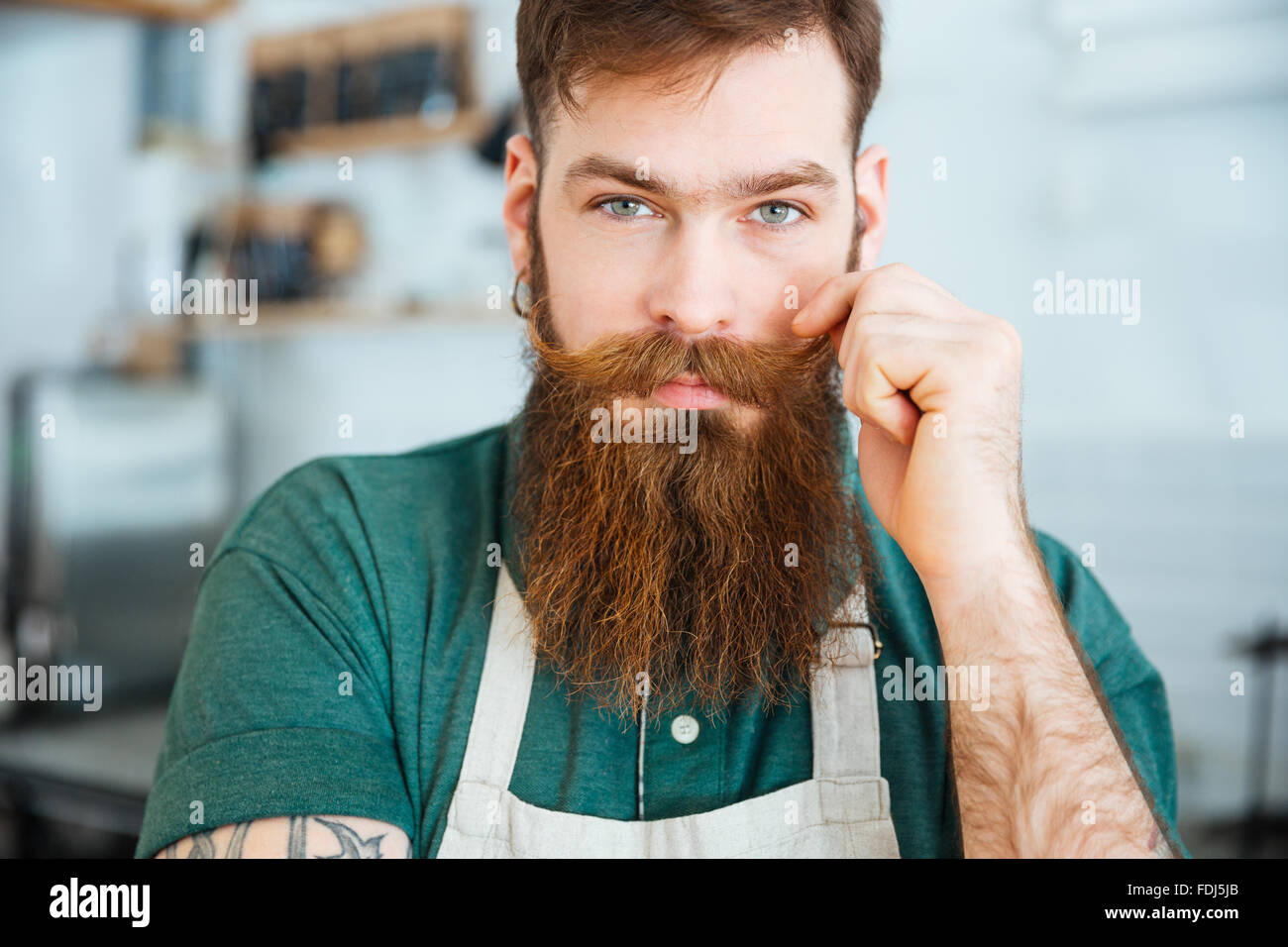 Closeup portrait of handsome young man with beard en tablier blanc de toucher sa moustache Banque D'Images