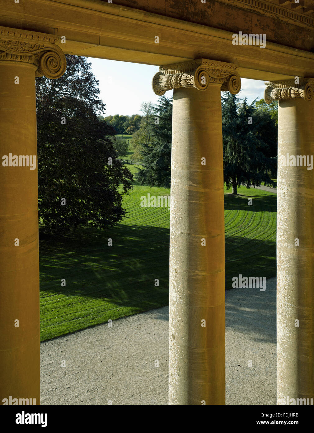 Une vue sur l'entrée de route à travers les piliers ioniques du portique en retrait sur l'avant de l'ouest du parc de Basildon, Berkshire. Banque D'Images