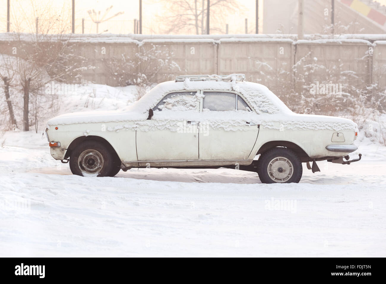 Voiture abandonnée couverte de neige en hiver au coucher du soleil, des tons chaleureux, vue de côté. La rouille, le recyclage, le traitement des métaux, la radiation de l'automobile. Banque D'Images