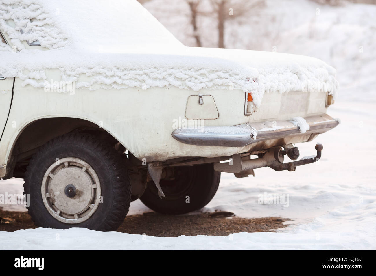 L'arrière du coffre de la voiture couverte de neige en hiver, l'ancienne couleur blanc cassé au coucher du soleil. Le recyclage, le traitement des métaux, la radiation de l'automobile. Banque D'Images