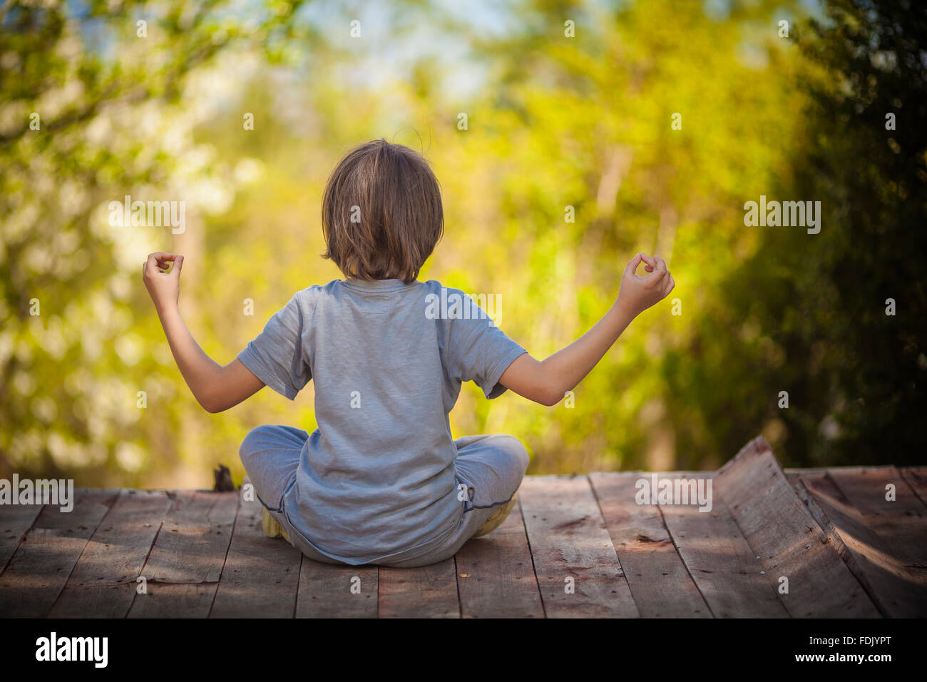 Vue arrière d'un garçon assis sur une terrasse en bois en méditant Banque D'Images