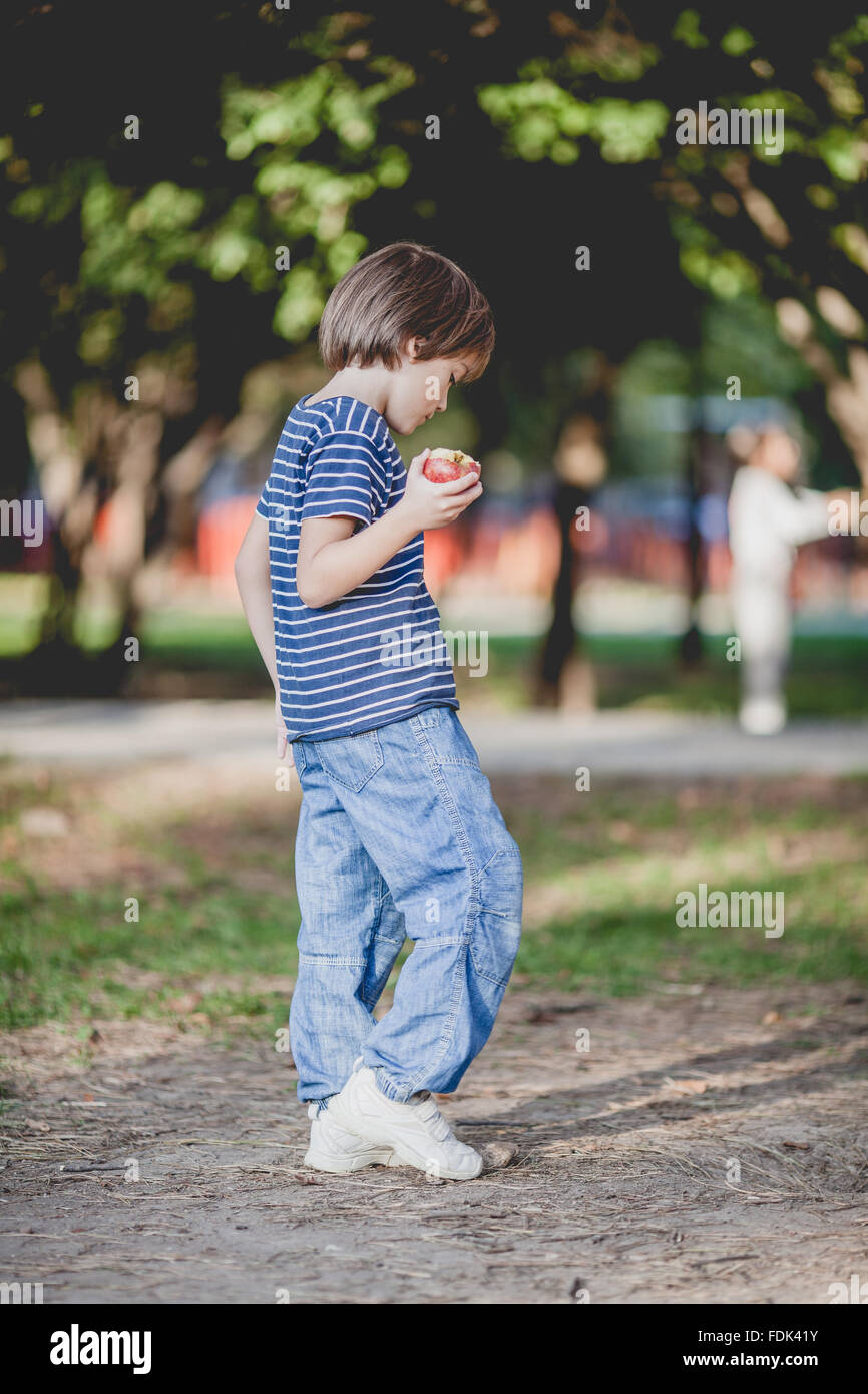 Boy standing in park manger une pomme Banque D'Images