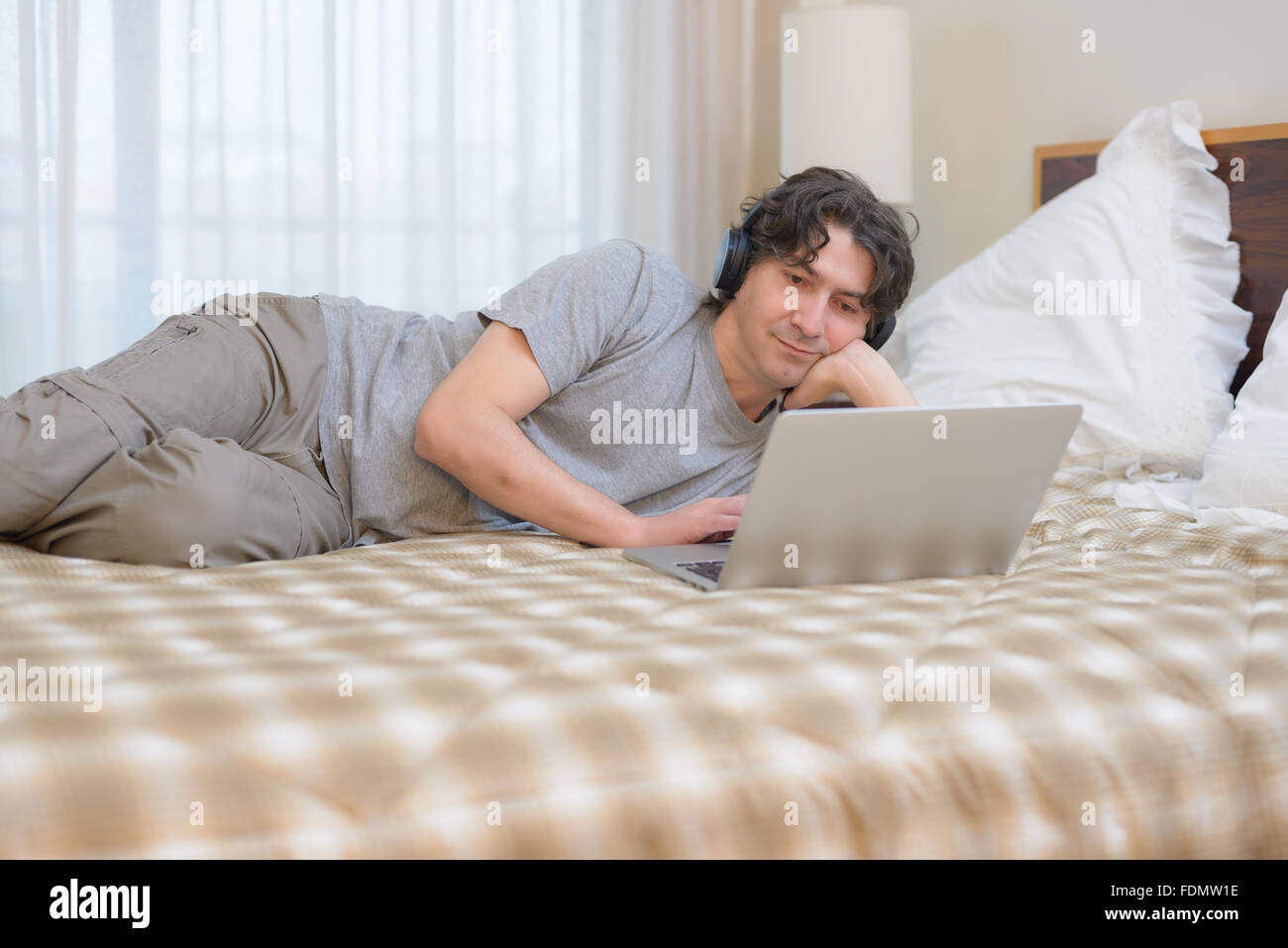 Homme couché lit à l'aide de l'ordinateur portable tout en écoutant de la musique avec des écouteurs Banque D'Images