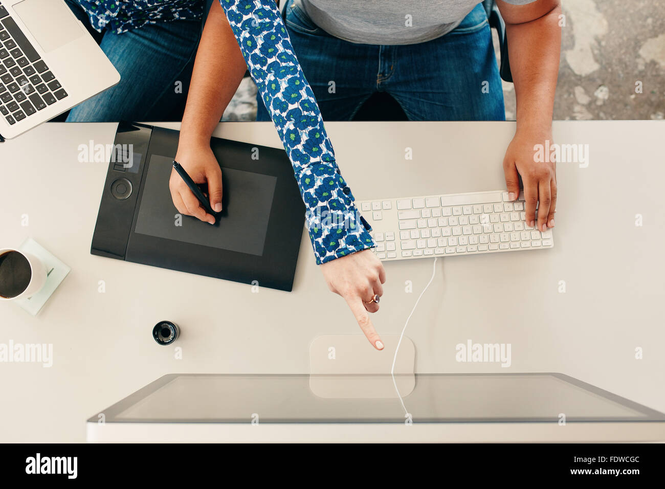 Vue de dessus cropped shot of a man using digital tablette graphique avec stylet et de l'ordinateur clavier, avec woman pointing at computer mo Banque D'Images