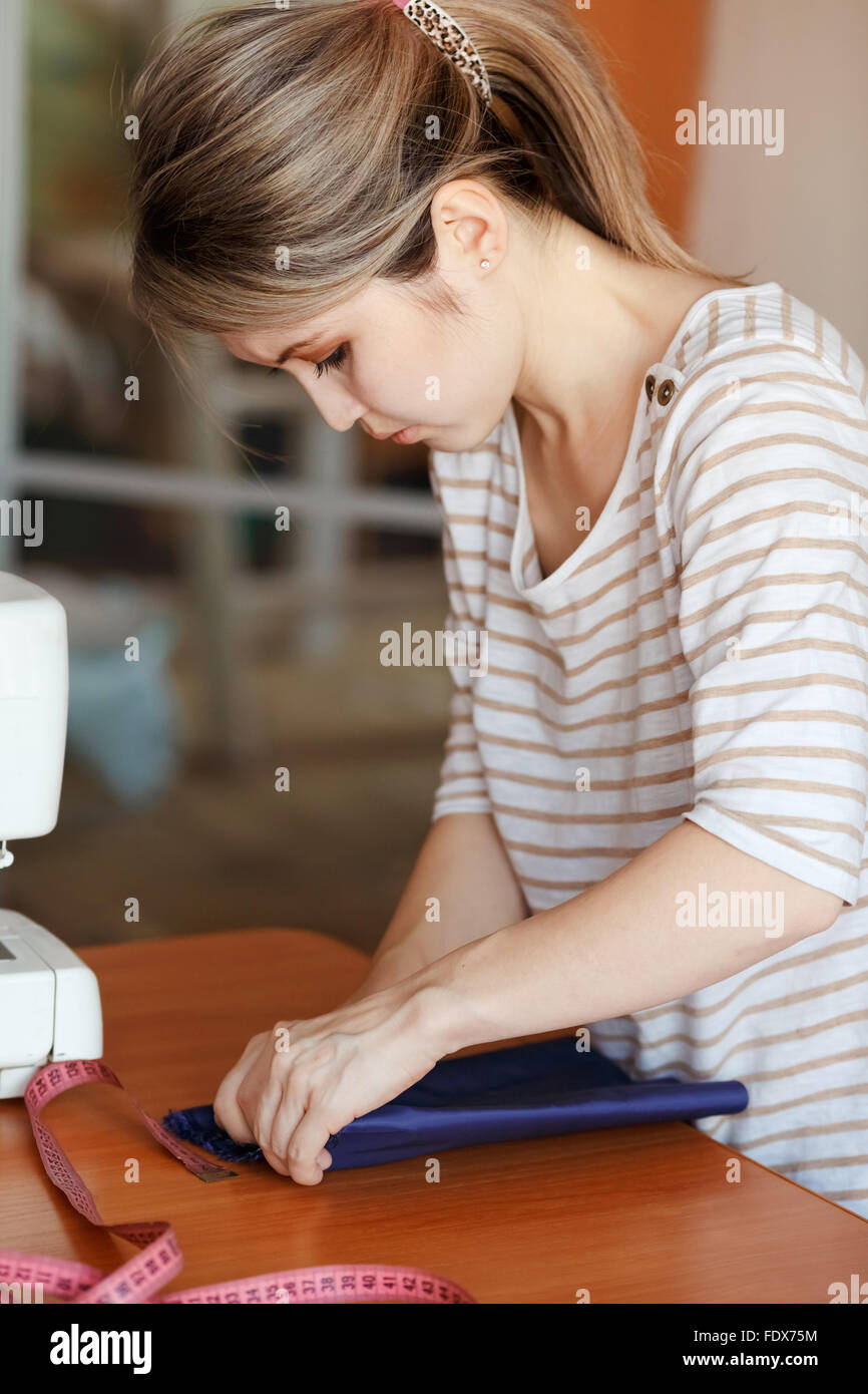 Jeune femme à la maison de couture, hemming tissu bleu. Fashion designer créant de nouveaux styles à la mode. Couturière vêtements fait par emploi à temps partiel. Banque D'Images