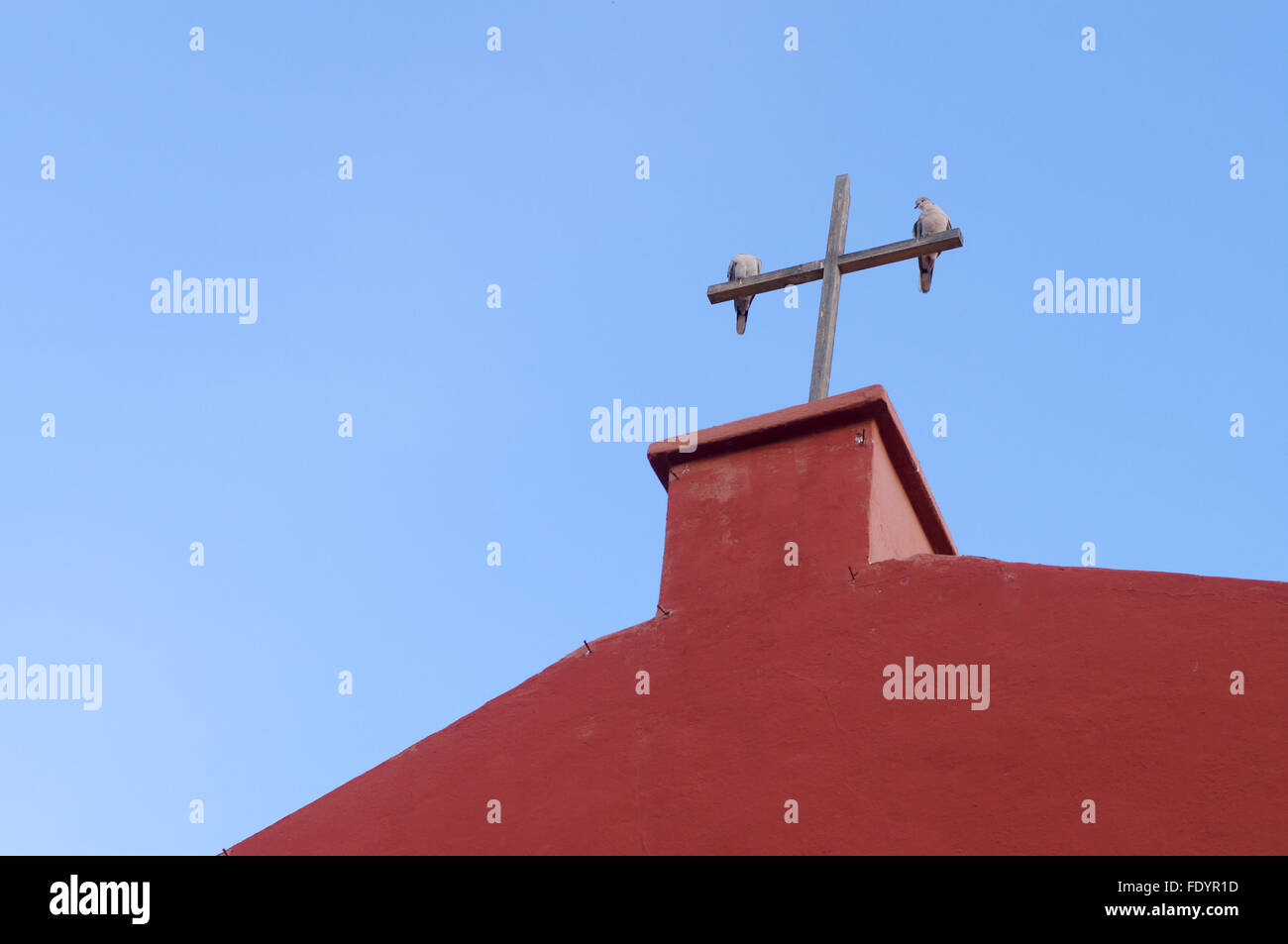 Deux pigeons sur la croix en bois d'église rouge contre le ciel bleu Banque D'Images