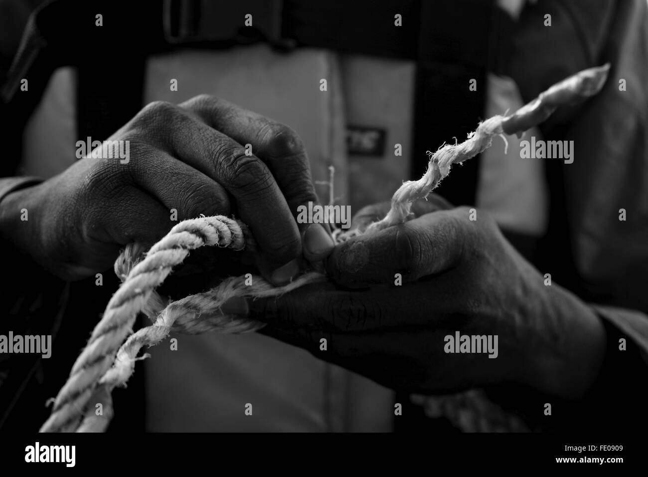 Détail en noir et blanc des mains de la connexion de deux morceaux de corde Banque D'Images