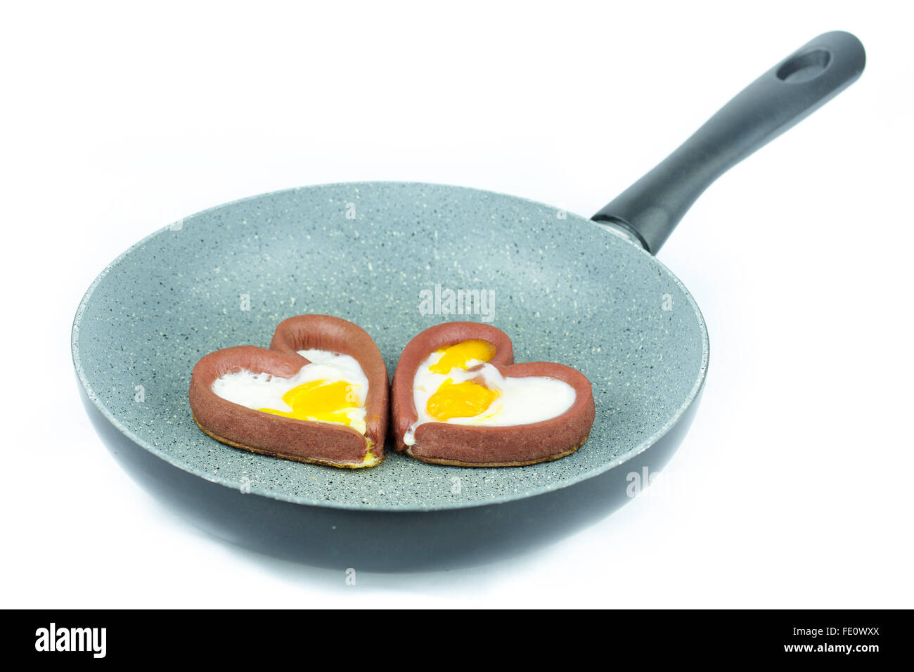 Couple d'oeufs la cuisson avec des saucisses en forme de cœur dans une poêle isolé sur fond blanc Banque D'Images