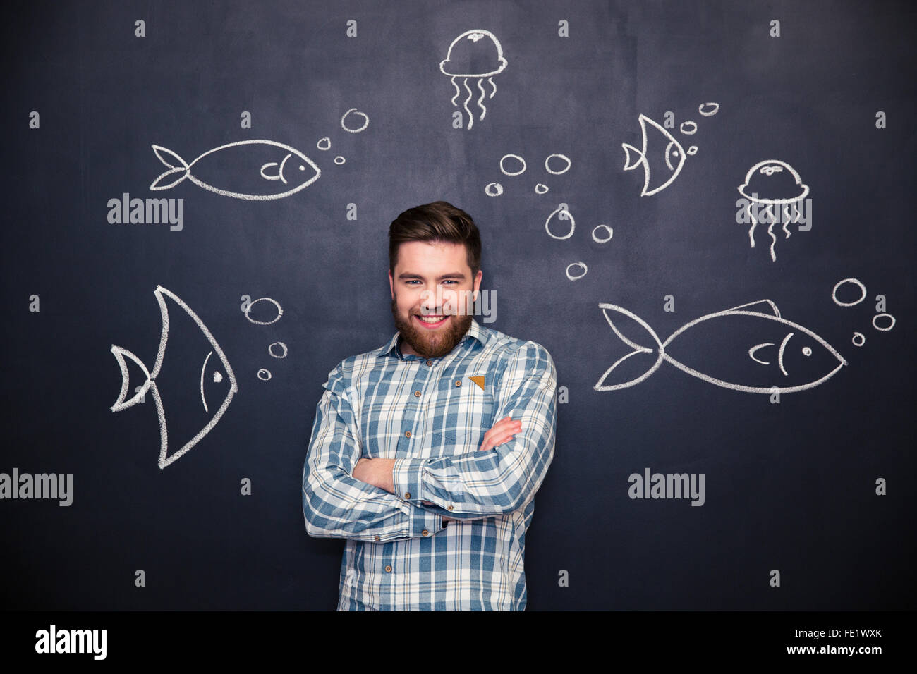 Cheerful handsome young man standing barbus avec les mains pliées sur tableau noir avec fond dessiné les poissons et méduses Banque D'Images