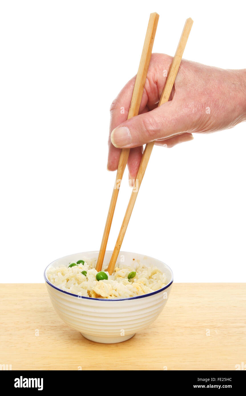 Main tenant les baguettes dans un bol de riz frit à l'oeuf sur une table contre un fond blanc Banque D'Images