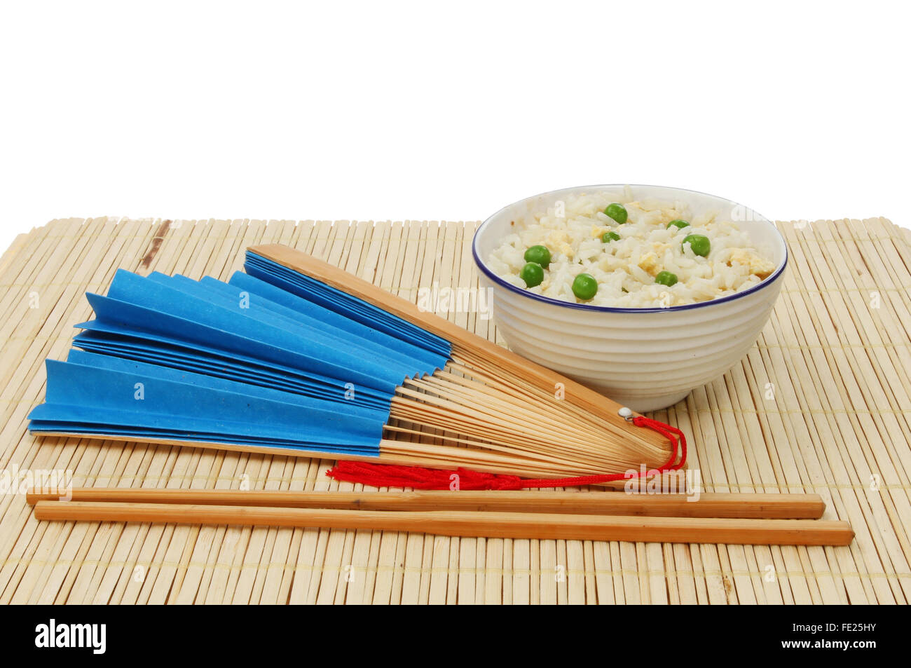 Repas asiatique, riz frit à l'oeuf dans un bol avec des baguettes et un ventilateur sur un papier bleu mat en bambou sur un fond blanc. Banque D'Images