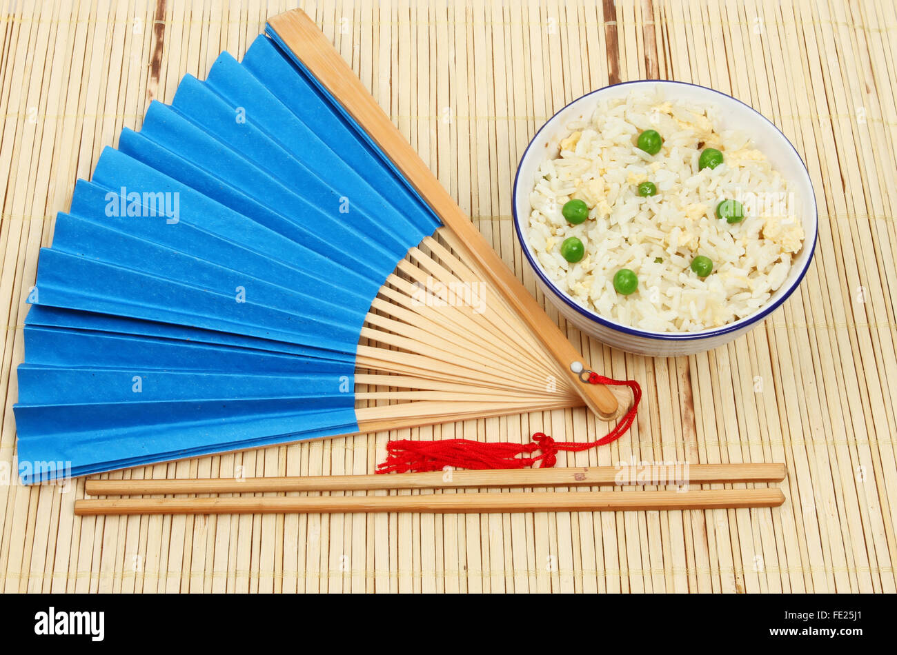 Repas Oriental, riz frit à l'oeuf dans un bol avec un ventilateur et baguettes sur un mat en bambou Banque D'Images