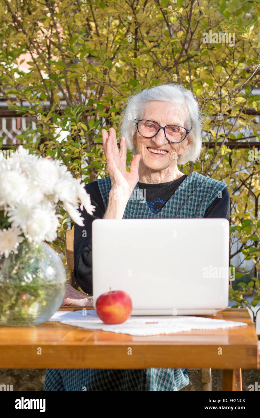 Femme de 90 ans tout en ayant un signe un appel vidéo sur un ordinateur portable blanc Banque D'Images