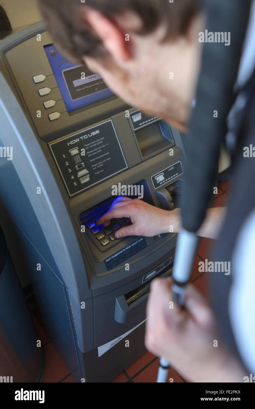 Jeune homme aveugle avec la canne à l'aide d'un distributeur automatique de banque Banque D'Images