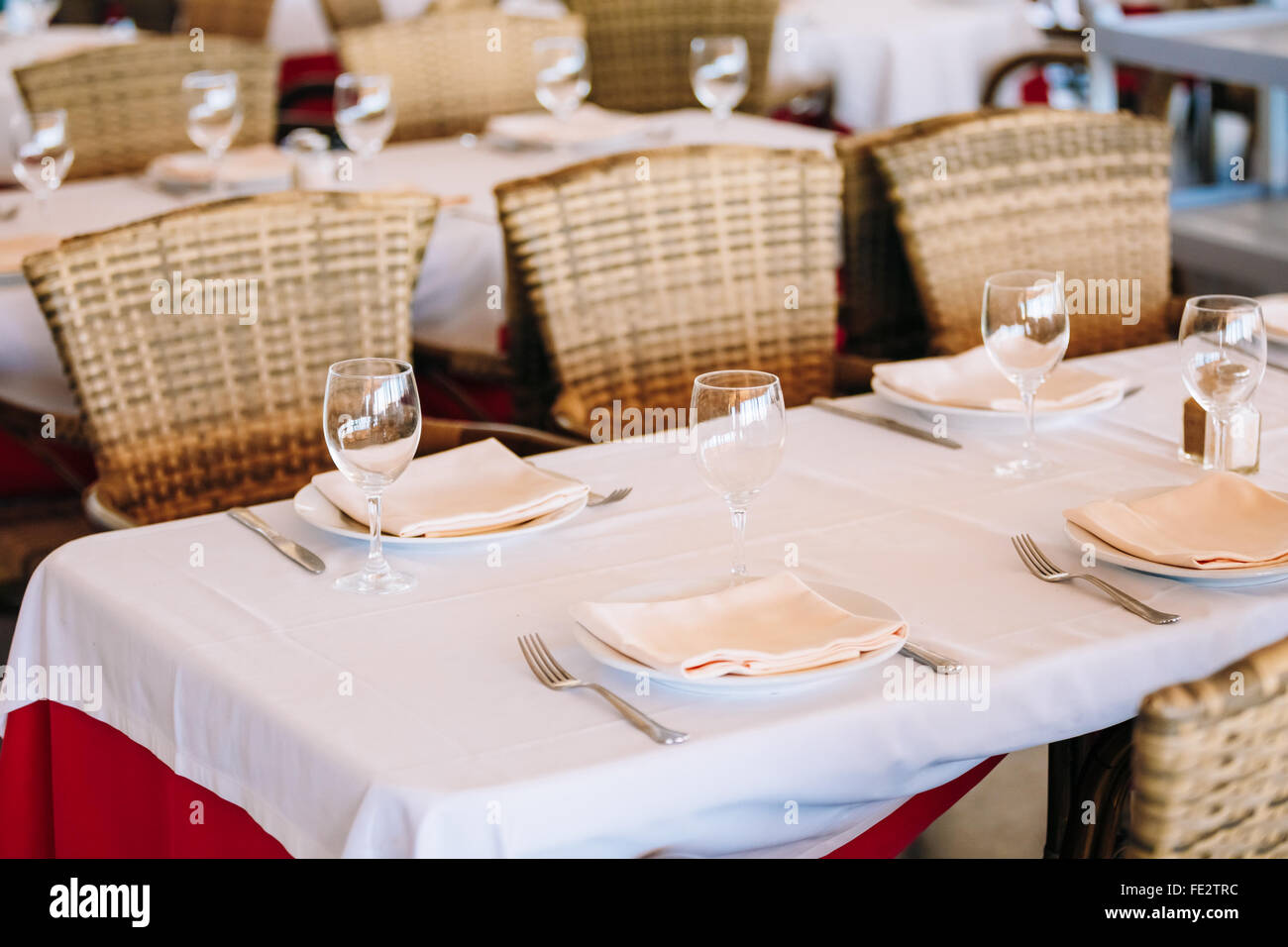 La simple discret de l'intérieur de l'abri de l'été, cafe tables avec nappes blanches et de chaises en osier. Restaurant européen. Banque D'Images