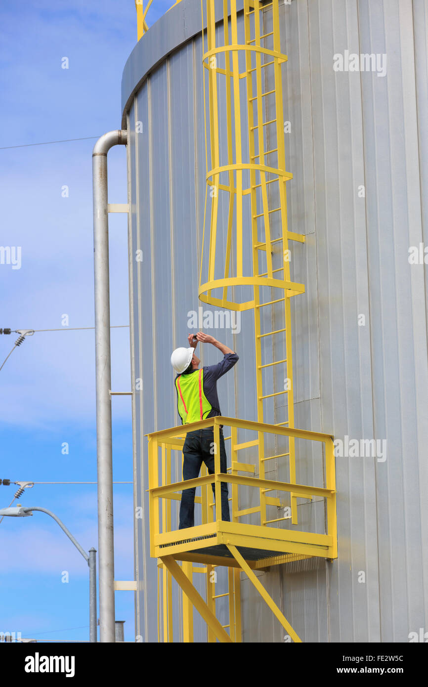 Ingénieur industriel de prendre une photo de la cage de sécurité sur un réservoir de stockage de carburant Banque D'Images