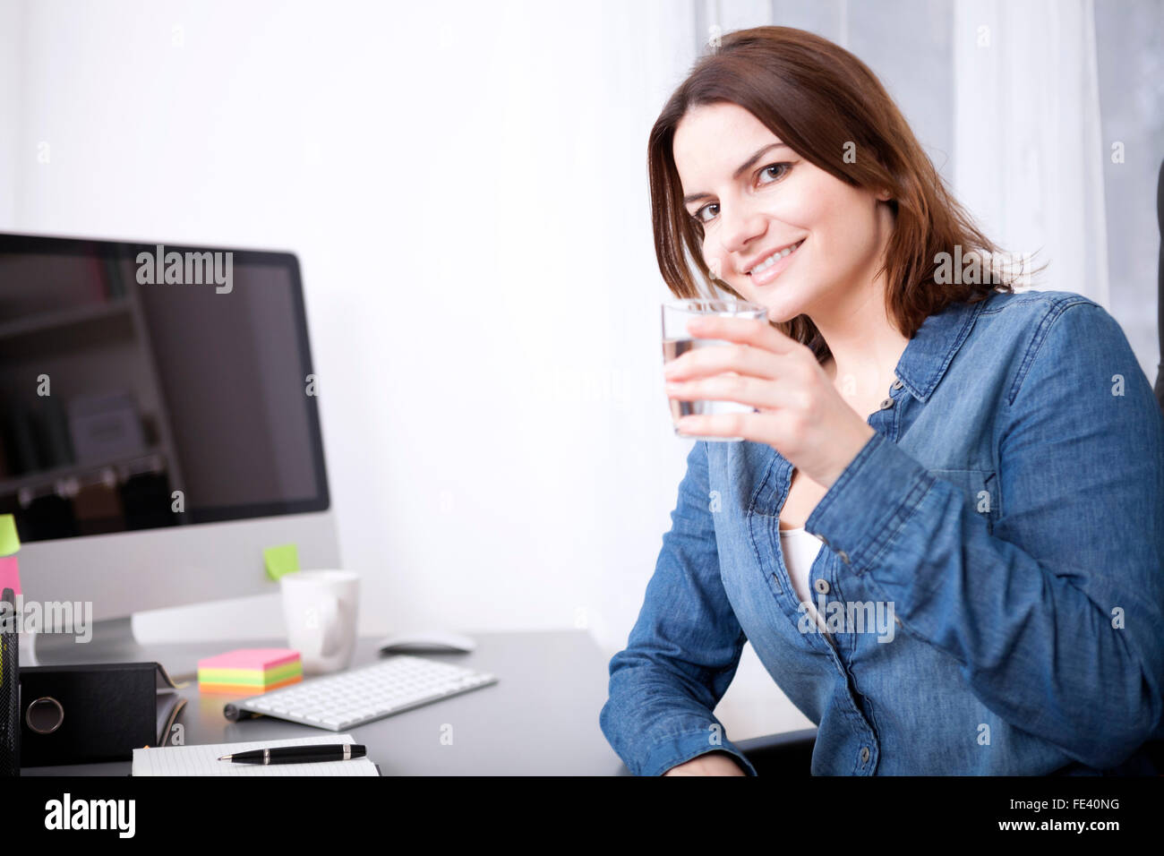 Close up Office de Femme tenant un verre de l'eau, appuyée sur son bureau en regardant la caméra. Banque D'Images