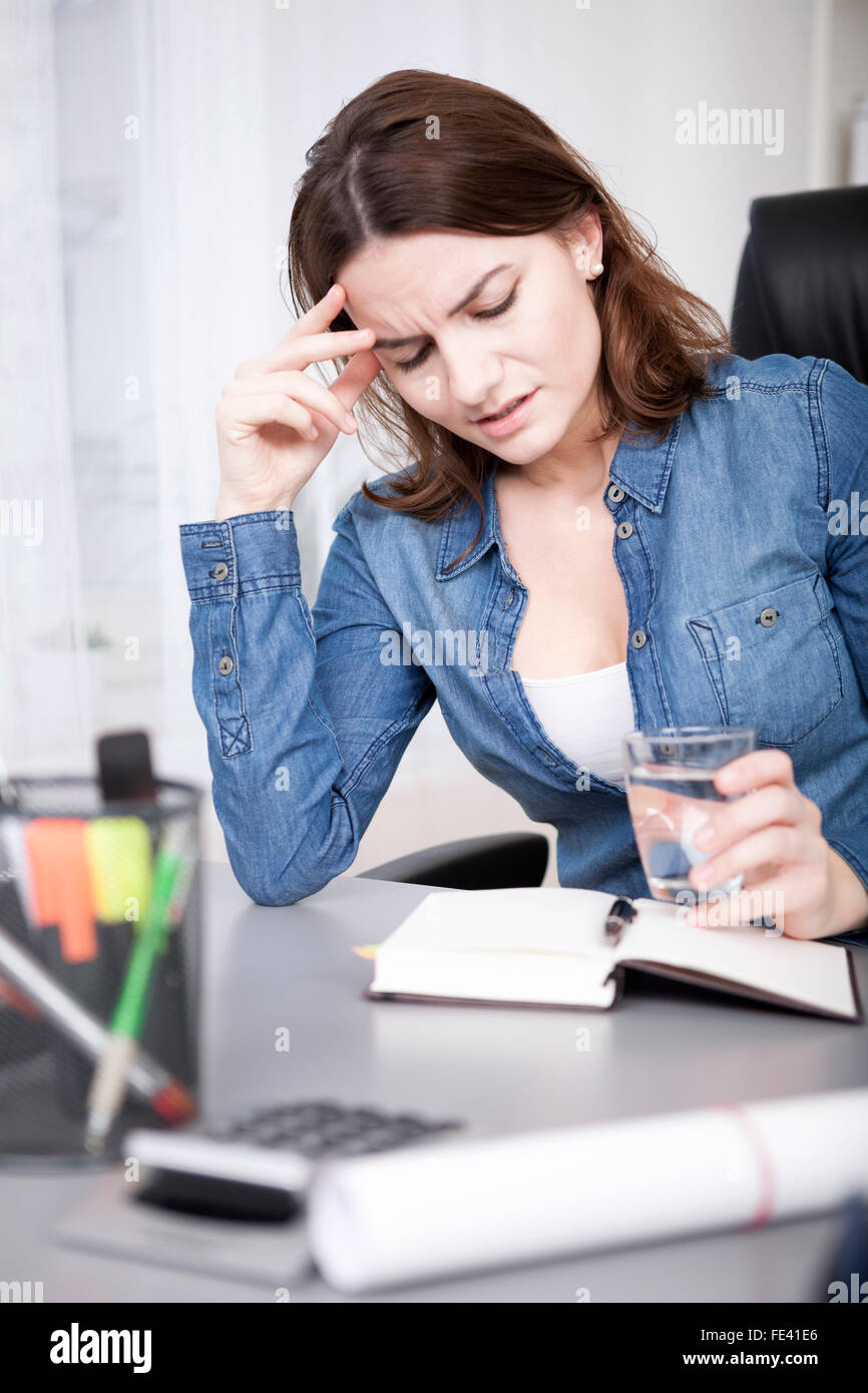 Close up Bureau des jeunes adultes femme lisant un livre au sérieux tout en tenant un verre d'eau à son bureau Banque D'Images