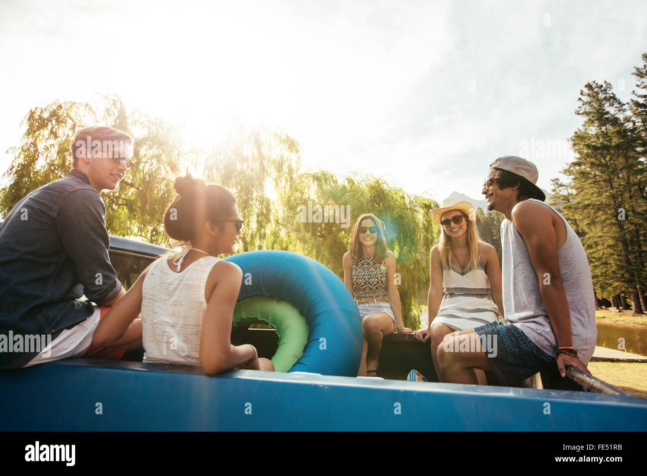Groupe de jeunes amis assis à l'arrière d'une camionnette avec des tubes gonflables passe un été de congé sur une journée ensoleillée. Banque D'Images