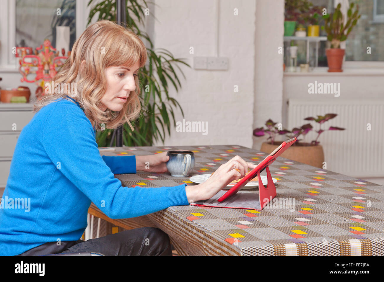 Femme à l'aide d'un iPad à une table du salon. Banque D'Images