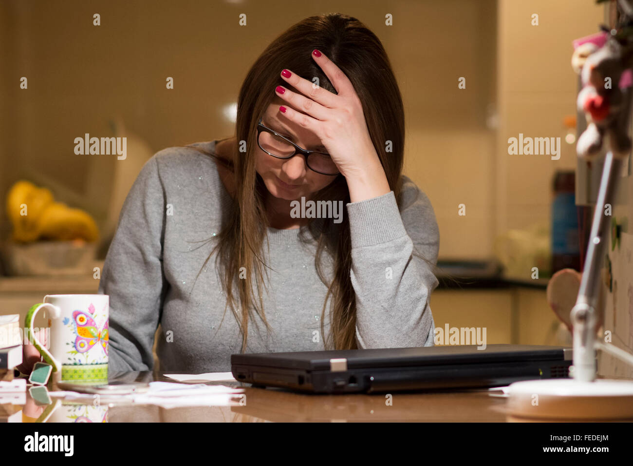 Jeune femme de payer les factures en ligne tard dans la soirée après avoir terminé tous les travaux de sa maison, assis au bureau avec ordinateur, b Banque D'Images