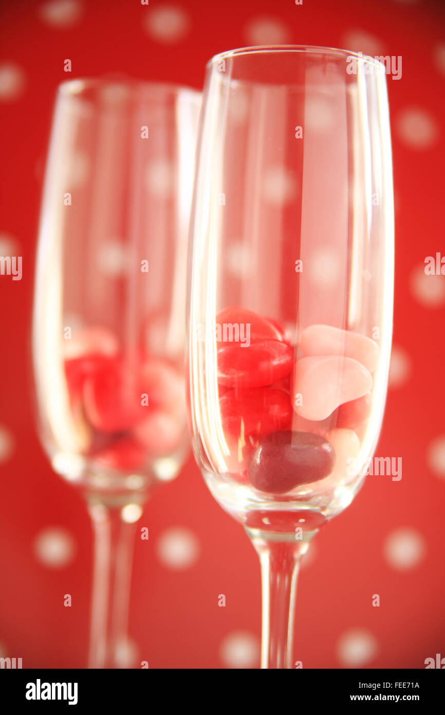 Deux flûtes de vin avec des bonbons coeurs rouge et blanc contre un fond à pois Banque D'Images