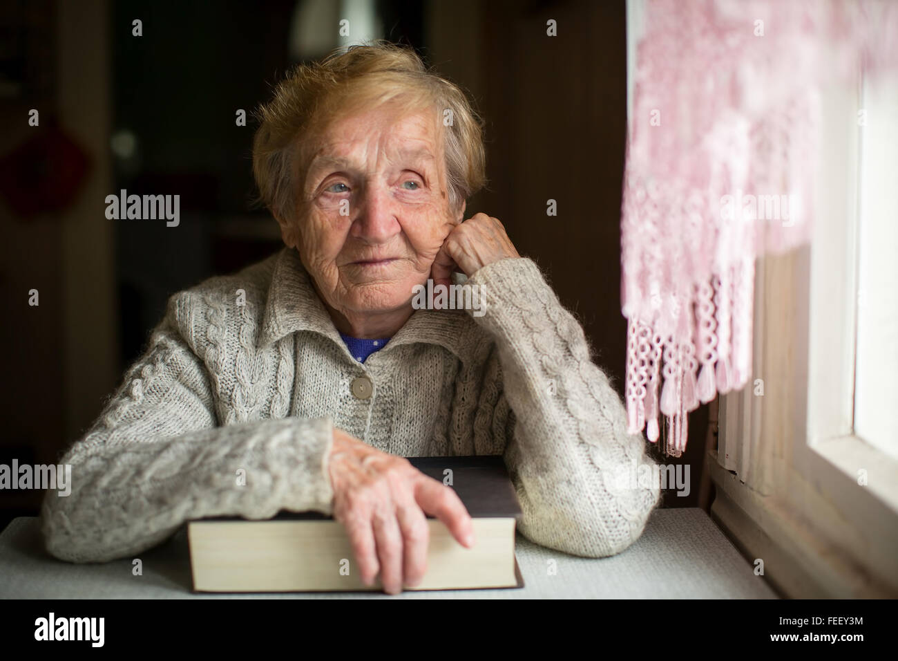 Une femme âgée est assise avec un grand livre près de la fenêtre. Banque D'Images