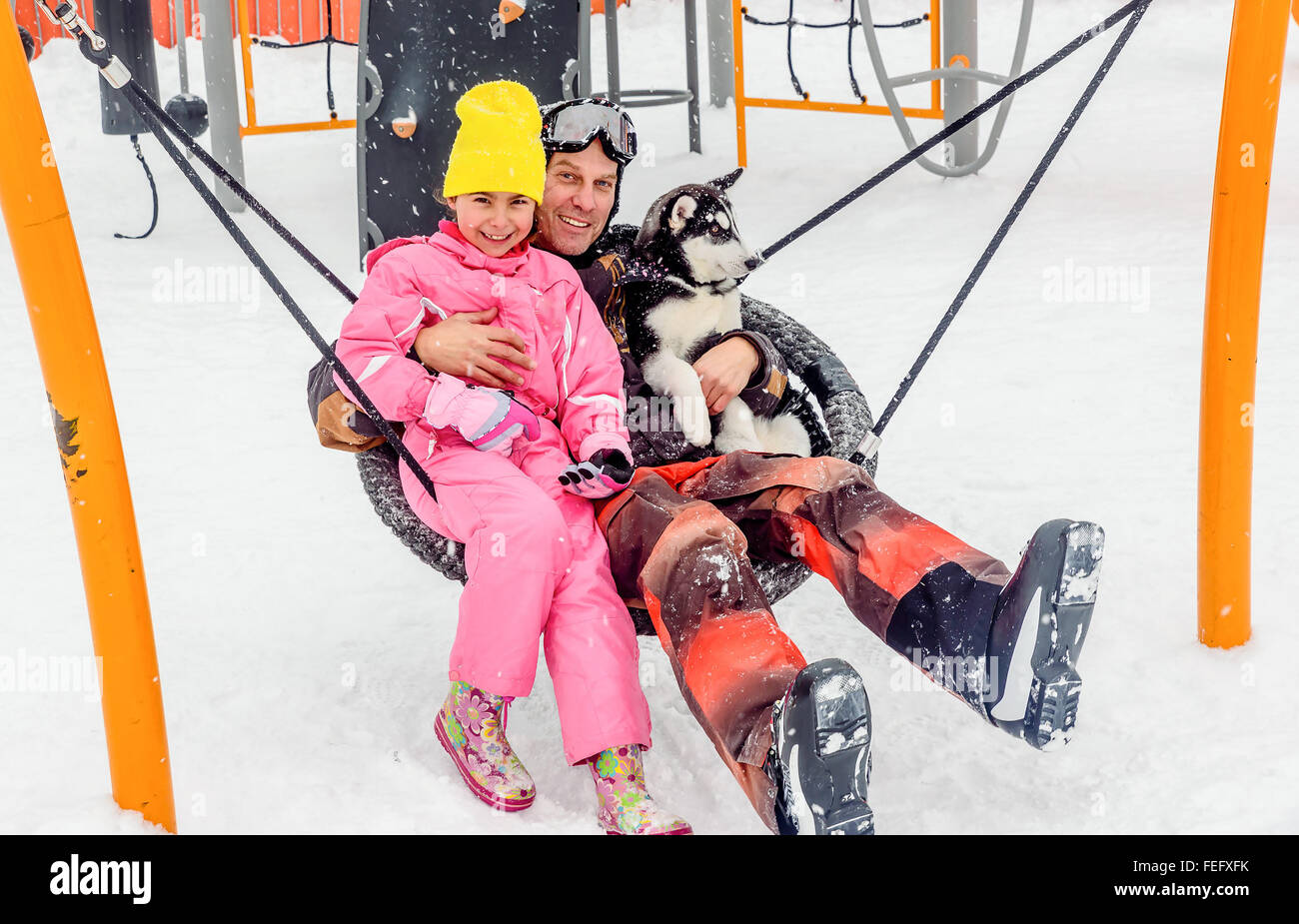 Homme assis sur la balançoire avec husky puppy dog et sa fille en hiver Banque D'Images