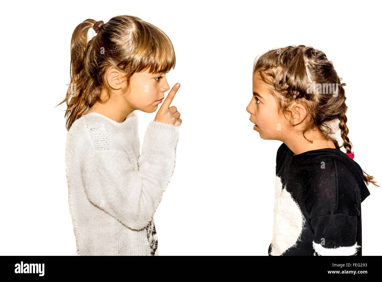 Petite fille dire à sa sœur de se taire avec son doigt sur la bouche. Un geste de silence . Closeup-Isolated on white Banque D'Images