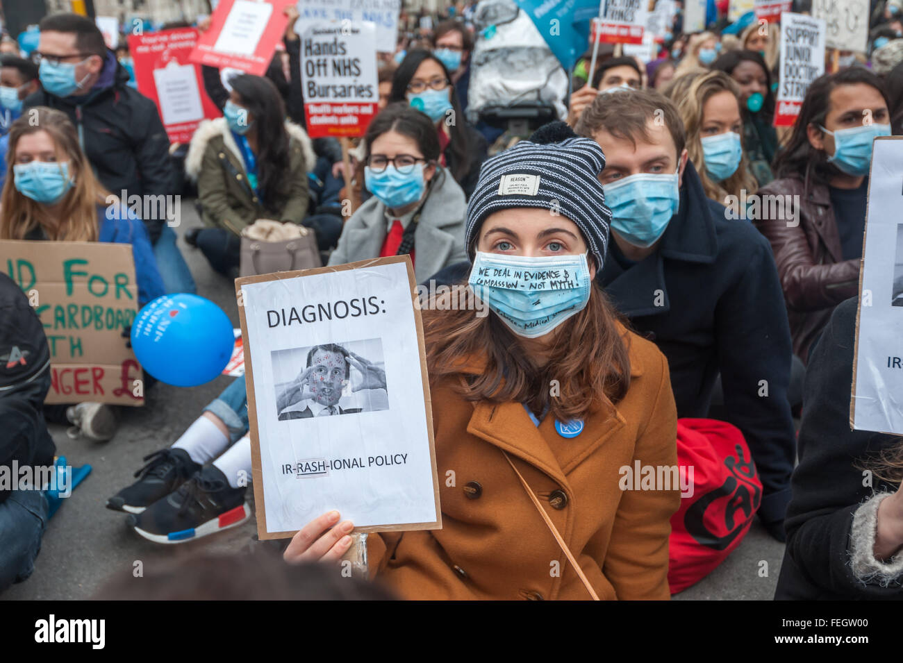 Londres, Royaume-Uni. 1er février 2016. Une femme dans la foule de plusieurs milliers de médecins s'asseoir le long de Whitehall à Downing St dans les masques chirurgicaux contre l'imposition de nouveaux contrats ils disent va détruire le NHS et le rendre dangereux pour les patients montrant une plaque hlds Jeremy Hunt's visage couvert de taches et le message "Diagnostic : IR-FESSIER-ER STRATÉGIE.' Les médecins accusent Jeremy Hunt de tromper le public et les médias et le message sur son masque est 'nous traiter en preuve et la compassion - Mythe pas !" Peter Marshall/Alamy Live News Banque D'Images