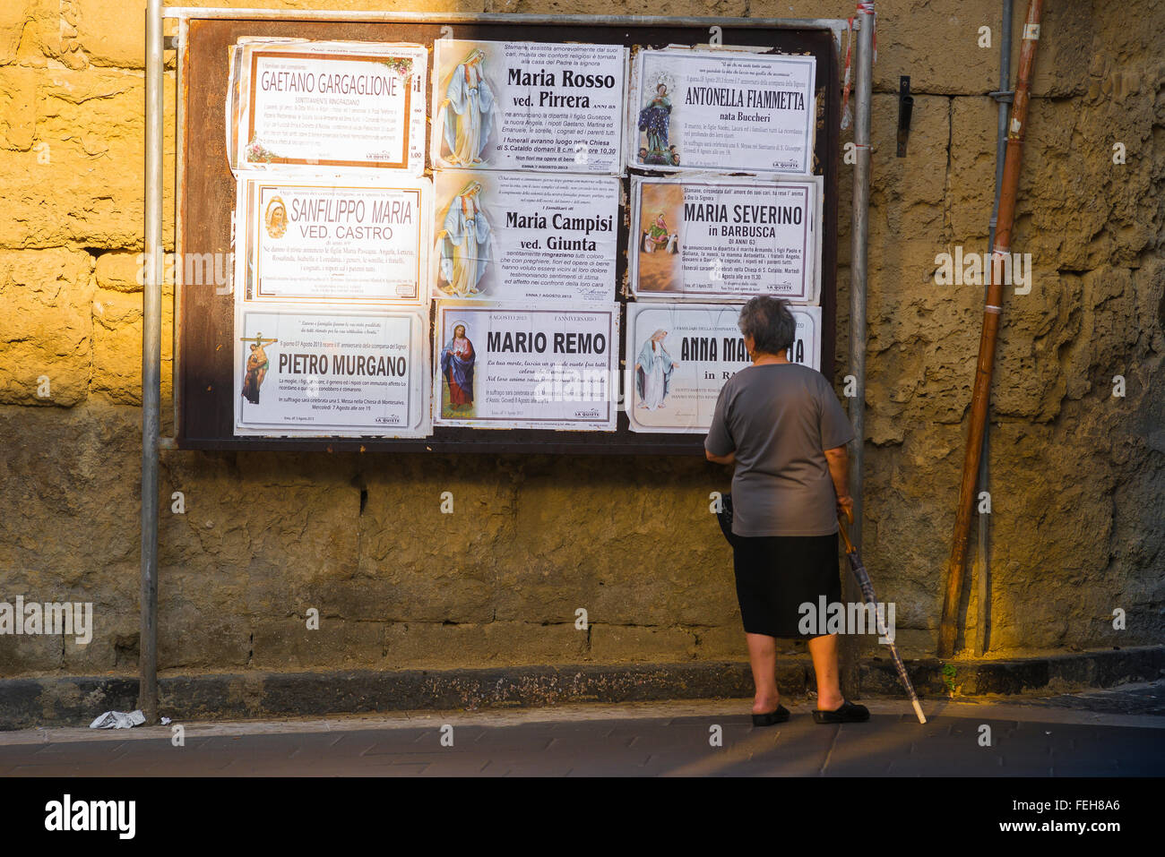 Femme âgée Italie, vue arrière d'une femme locale âgée à Enna, Sicile, s'arrête pour lire les dernières notifications publiques de funérailles dans la communauté. Banque D'Images