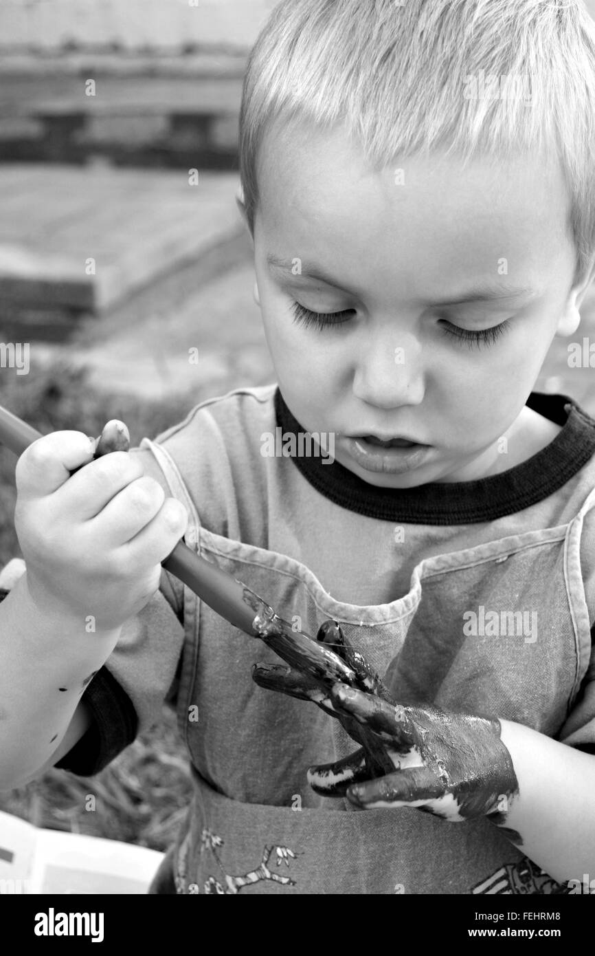 Peinture enfant blond sa propre main à l'aide d'un pinceau, en noir et blanc. Banque D'Images