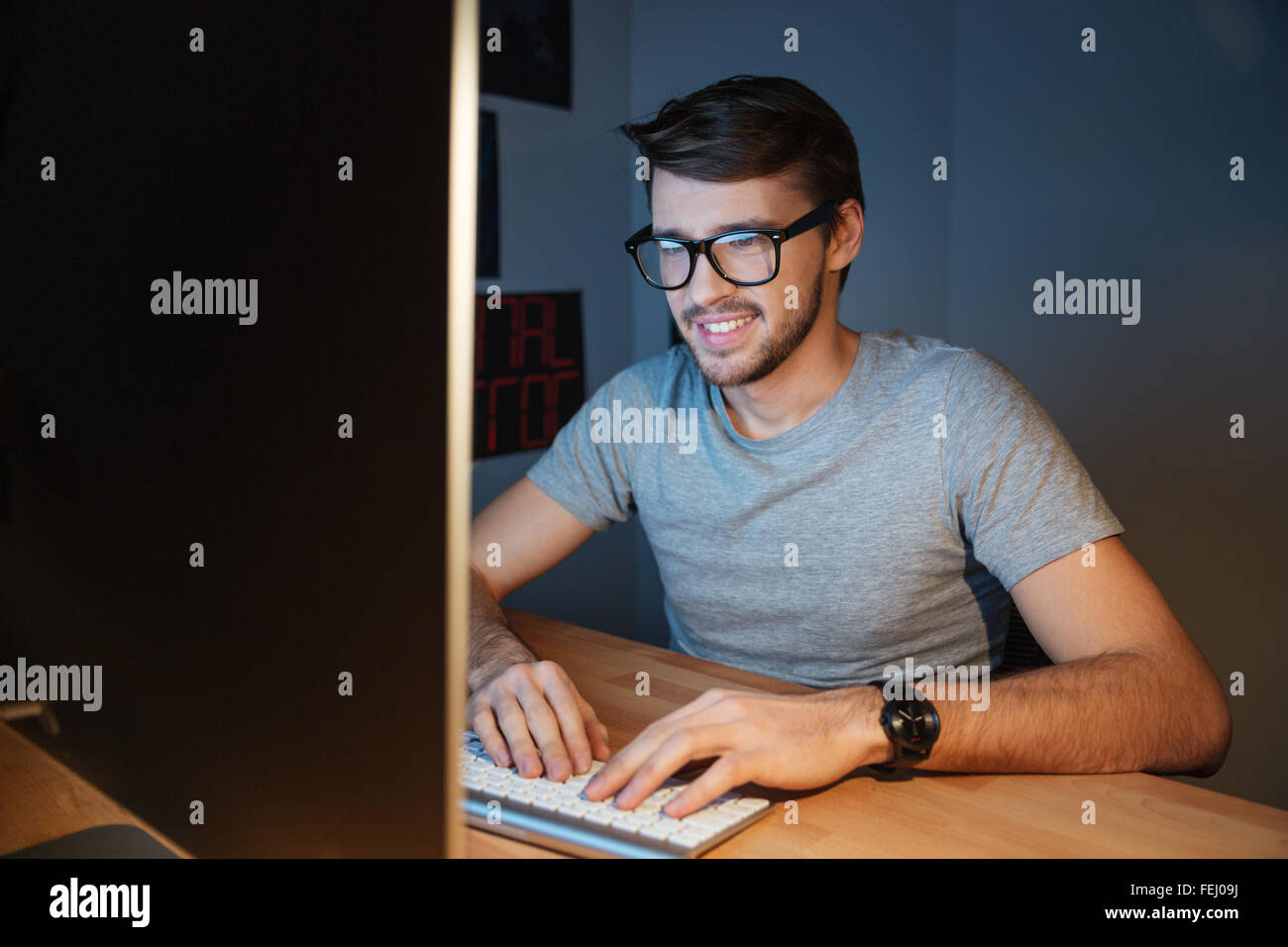 Heureux jeune homme attrayant dans les verres assis et de la saisie sur ordinateur à la maison Banque D'Images