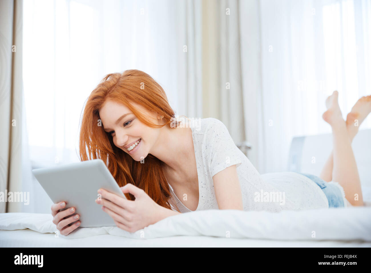 Smiling redhead woman using tablet computer on le lit à la maison Banque D'Images