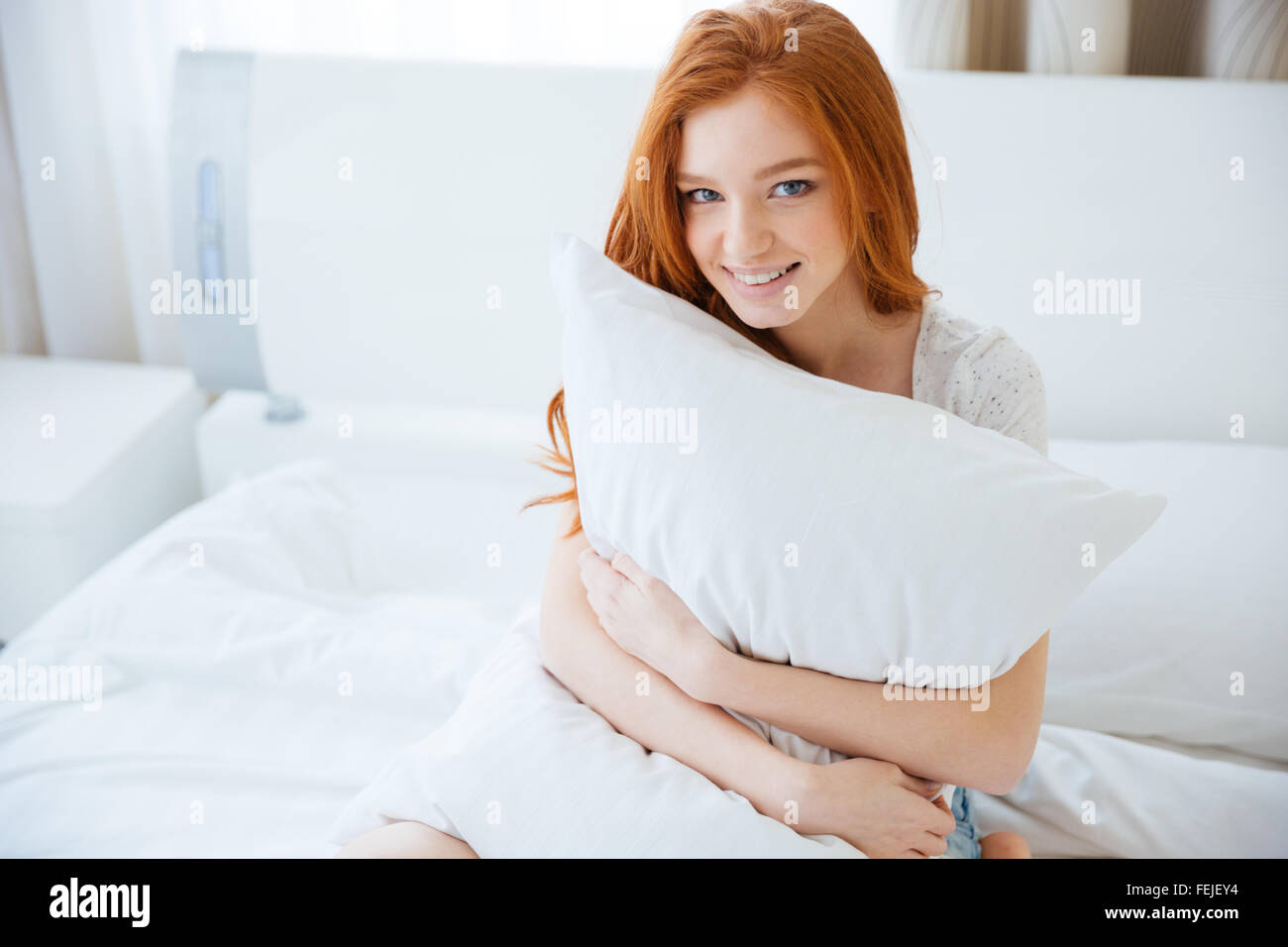 Heureux redhead woman holding oreiller sur le lit à la maison Banque D'Images