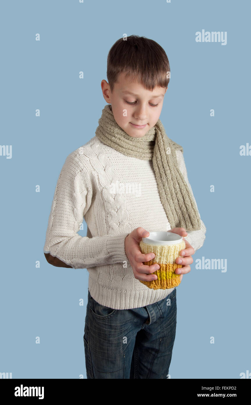 Cute boy en blanc pull et écharpe verte avec une tasse blanche sur fond bleu Banque D'Images