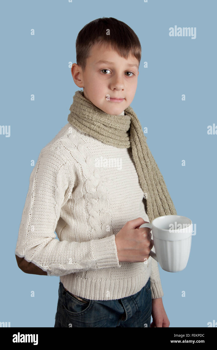 Cute boy en blanc pull et écharpe verte avec une tasse blanc isolé sur fond bleu Banque D'Images