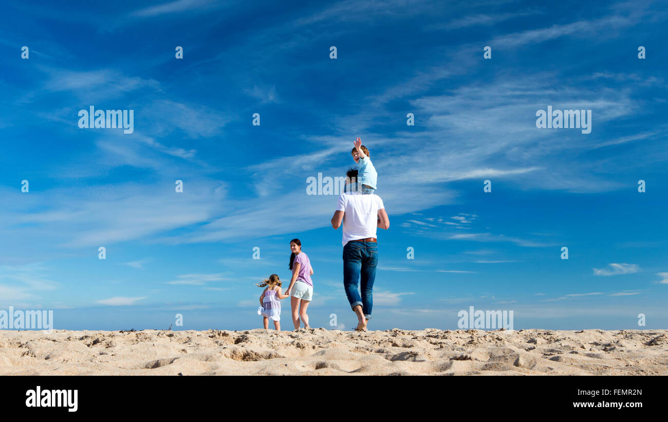 Famille de quatre à pied jusqu'à la côte. Le petit garçon est sur le dos des pères et brandit à l'appareil photo. Banque D'Images