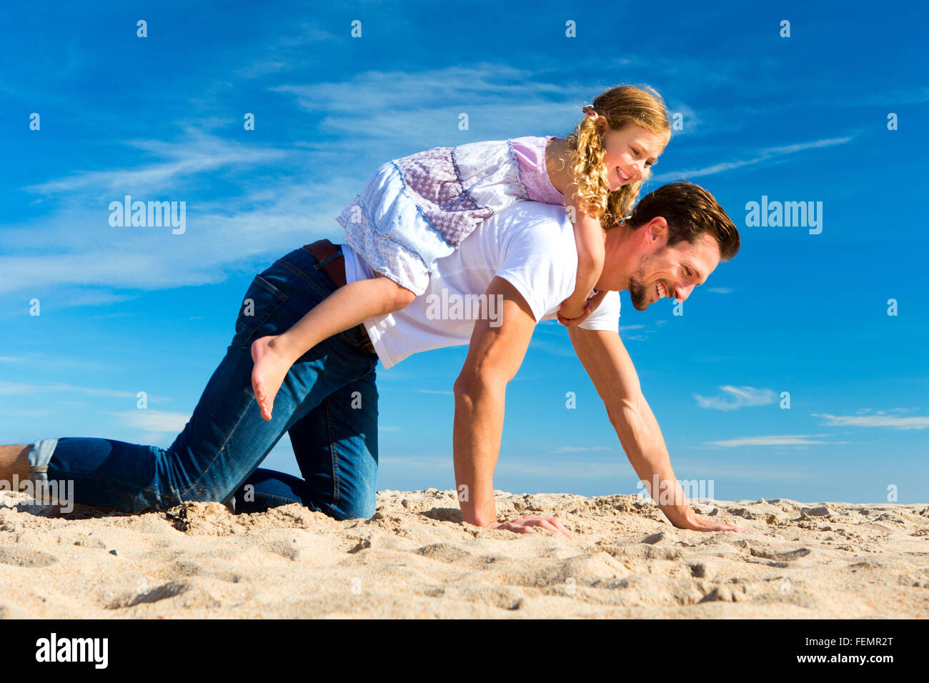 Père en portant sa fille sur son dos sur le sable sur la plage. Banque D'Images