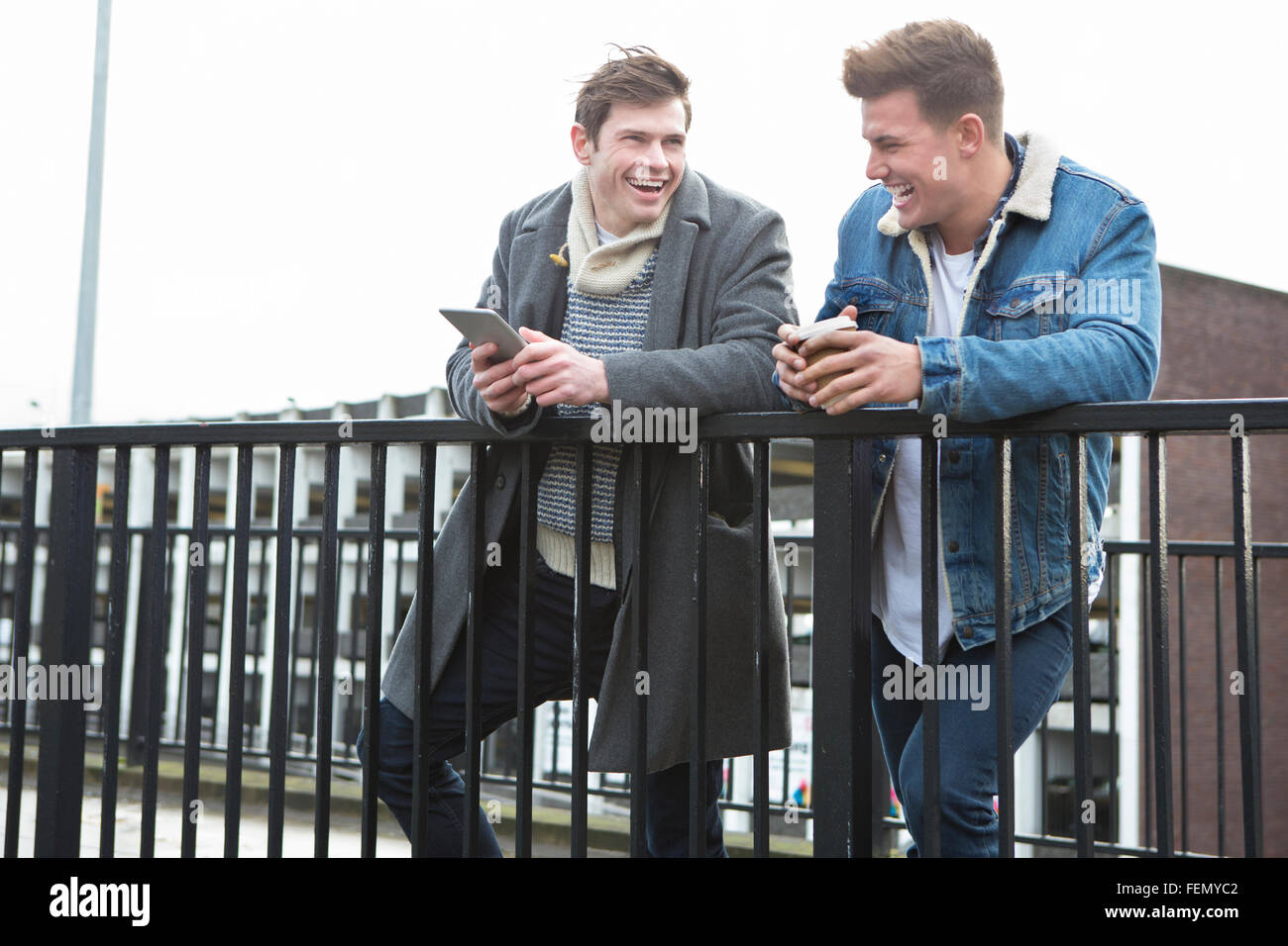 Deux jeunes hommes parlant de la ville. L'un est titulaire d'un smartphone, l'autre tenant une tasse de café à usage unique. Banque D'Images