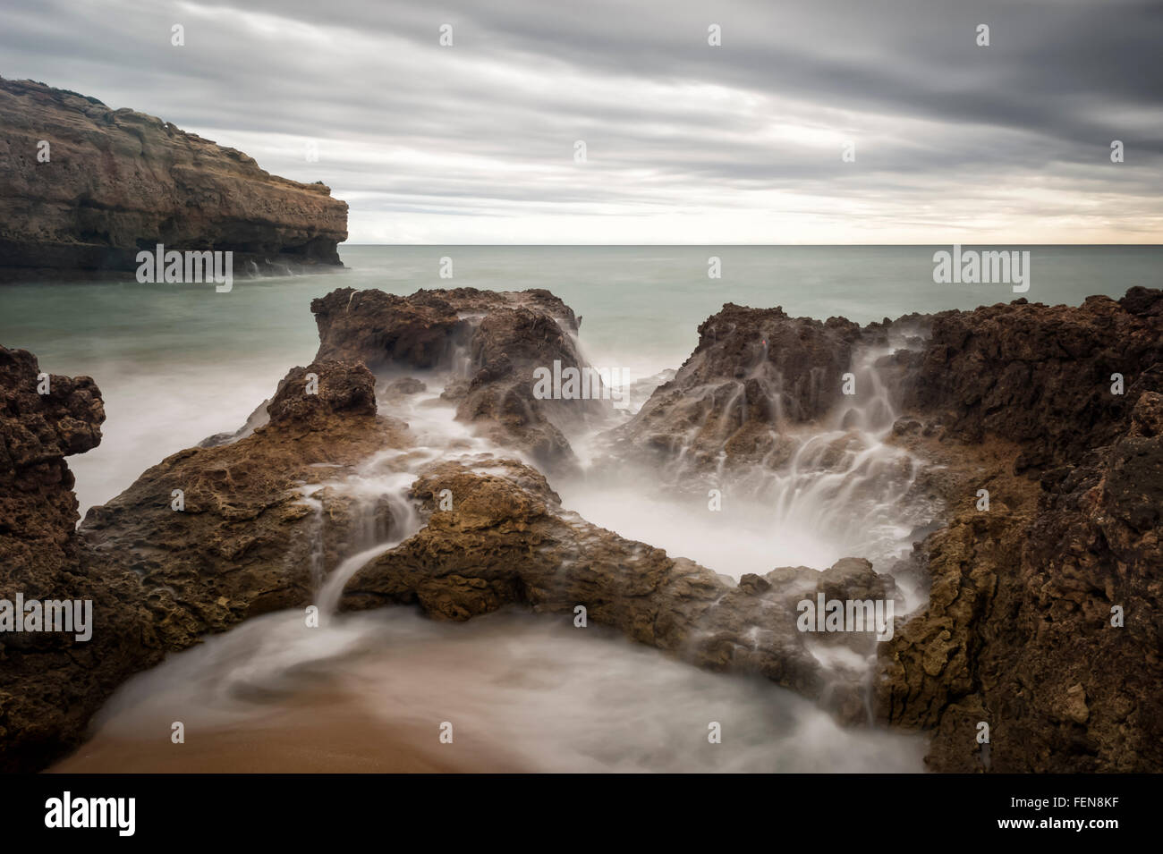 La longue exposition des vagues sur les rochers à Praia de Albandeira dans Portugal Banque D'Images